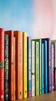 Colorful hardcover books arranged in a row on wooden shelf against soft blue and pink gradient background, suitable for education, library, and publishing designs.