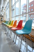 Colorful modern chairs lined up along large windows in bright contemporary waiting area, creating vibrant rainbow effect against urban backdrop.