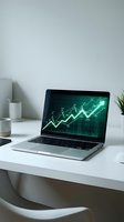 Laptop displaying green financial charts and stock market data on modern white desk workspace for business analysis and trading applications.