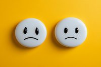 Two sad white emoji faces on vibrant yellow background. Minimalist composition showing negative emotions, depression, and mental health concept for social media content.