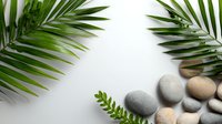 Fresh palm leaves frame smooth spa stones and delicate ferns on white background, creating zen-like composition for wellness and relaxation designs.