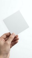 Hand holding blank white square paper card against light background for mockup design presentations.