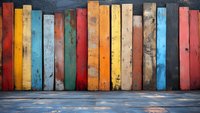 Colorful weathered wooden planks forming wall background with rustic texture and peeling paint in yellow, red, blue, and green shades against concrete floor.