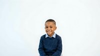 Young boy with dark skin tone and short hair, wearing a navy blue knit sweater with white collar, smiling at camera against white background. Isolated portrait for educational, family, and commercial design use.