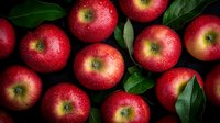 Fresh red apples with water drops and green leaves on dark background, macro shot of ripe organic fruit arranged in natural composition.