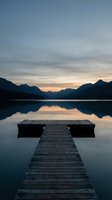 Wooden dock extending into calm lake at sunset with mountain silhouettes reflected in water creating peaceful atmosphere for meditation and relaxation.