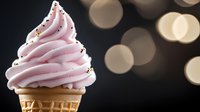 Soft pink swirled ice cream cone topped with sprinkles against dark background with golden bokeh lights creating festive mood for dessert and food photography.