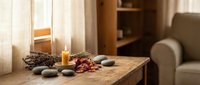 Cozy spa wellness setup with burning candle, smooth stones, dried flowers and natural decorations on wooden table in warm sunlit room for relaxation.