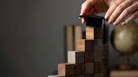 Businessman hands stacking wooden blocks building tower structure for strategic planning and growth concept in modern office environment.