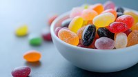 Colorful sugar coated jelly beans candy in white ceramic bowl on dark background with selective focus and copy space for confectionery design.