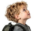 Young boy with curly blonde hair wearing backpack and gray sweater looking up with wonder and curiosity against white background, profile view. Isolated portrait for education and childhood concepts.
