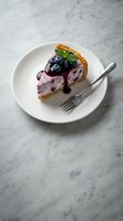 Blueberry cheesecake slice with fresh berries and mint garnish on white plate with fork, marble background for bakery menu and dessert photography.