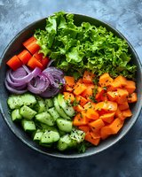 Fresh colorful vegetable bowl with lettuce, cucumber, carrots, bell peppers and red onion arranged in dark plate for healthy eating and meal prep.
