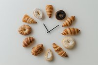 Freshly baked croissants and donuts arranged in a clock shape on a light background, symbolizing breakfast time and morning bakery concept.