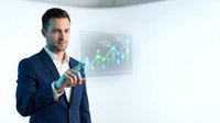 Professional businessman in dark suit touching holographic financial chart with upward trending graphs and data visualization in modern office environment.