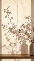 Delicate branch with small flowers in ceramic vase casting soft shadows on warm beige wall creating peaceful minimalist home decor atmosphere.