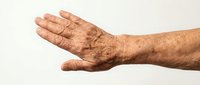 Senior male hand with age spots and wrinkles extended in open palm gesture against neutral background, representing aging, experience, and human vulnerability.