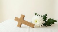Wooden cross with white chrysanthemum flower on soft fabric background for memorial, funeral, religious ceremony, sympathy card, condolence message design.