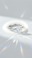 Elegant diamond solitaire engagement ring with brilliant cut stone on white gold band creating rainbow light reflections on pristine white surface.