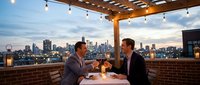 Two men in suits toasting with wine glasses on a rooftop restaurant at dusk, city skyline glowing in the background under string lights.