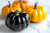 Fresh black and orange decorative mini pumpkins on white marble background, seasonal autumn harvest produce for Halloween and fall celebrations.