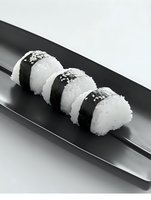 Fresh onigiri rice balls wrapped in nori seaweed with sesame seeds served on black rectangular plate. Traditional Japanese cuisine in minimalist style.