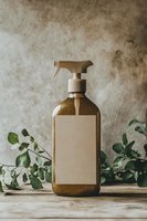 Amber glass spray bottle with blank label on wooden surface, decorated with eucalyptus leaves. Natural eco-friendly cleaning concept against textured wall.