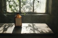 Amber glass bottle on wooden windowsill with natural sunlight casting leaf shadows through window, creating moody atmospheric composition.