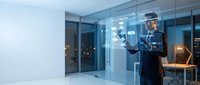 Professional security guard in uniform monitoring modern office building entrance with digital tablet technology for surveillance and access control.