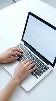 Hands typing on laptop computer keyboard at white desk workspace for remote work and digital productivity.