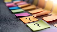 Colorful sticky notes with question marks arranged on dark wooden surface, selective focus on question marks creates depth and mystery for business concepts.
