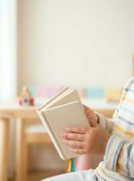 Child holding open book with colorful bookmarks in bright classroom setting, promoting early literacy, education, and reading development for young learners.