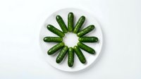 Fresh green cucumbers arranged in circular pattern on white plate, isolated on white background. Suitable for food photography, healthy eating, organic produce, culinary design.