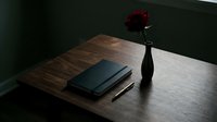 Minimalist wooden desk setup with closed notebook, pen and red rose in dark vase creating elegant workspace atmosphere for productivity and inspiration.
