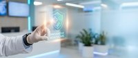 Businessman hand touching holographic shield icon with cybersecurity text in modern office environment, representing data protection and network security solutions.