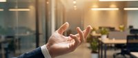 Businessman in office reaching out hand gesture for connection, teamwork, or agreement with warm golden light and modern workspace background.
