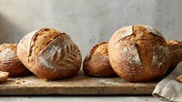 Fresh artisan sourdough bread loaves with golden crust on rustic wooden board, perfect for bakery marketing and culinary content creation.