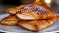 Golden brown crepes filled with creamy white filling stacked on plate, homemade breakfast pastry with powdered sugar dusting for food photography and menu design.