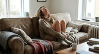 Young woman relaxing on comfortable leather sofa at home, enjoying peaceful moment in cozy living room with natural light streaming through windows.