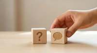 Hand placing wooden cube with brain symbol next to question mark block on table representing problem solving and decision making process.