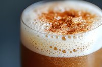 Creamy cappuccino topped with thick milk foam and dusted cinnamon powder, close-up view showing rich texture and bubbles against dark background.
