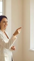 Professional businesswoman in white suit pointing forward with confident smile in bright office interior for corporate presentations and leadership concepts.