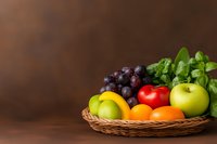 Fresh seasonal fruits and vegetables arranged in woven basket on wooden table with dark brown background, featuring apples, oranges, grapes, tomatoes and basil leaves.