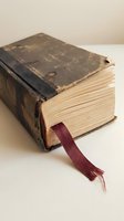 Antique leather-bound book with worn dark cover, aged cream pages, and burgundy ribbon bookmark displayed on white surface for literature and history concepts.