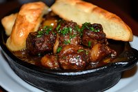 Tender beef tips braised in rich brown sauce, garnished with fresh herbs and served in cast iron skillet with crusty bread for restaurant menu or food blog.