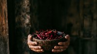 Hands holding wooden bowl filled with fresh red currants against dark rustic background, suitable for food photography, culinary blogs, and harvest themes.