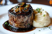 Grilled beef tenderloin steak topped with sauteed mushrooms in red wine sauce, served with creamy mashed potatoes and fresh herbs on white plate.