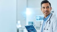 Professional Hispanic male doctor with stethoscope holding tablet displaying medical data in modern hospital setting for healthcare technology concepts.
