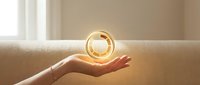 Woman's hand holding glowing light bulb on sofa, symbolizing ideas, innovation, and energy solutions for business and sustainability concepts.