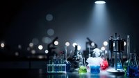 Laboratory glassware with colorful chemical solutions under dramatic spotlight illumination on dark background for scientific research and education.